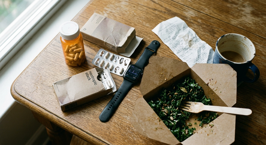 Flatlay of pharmacy focus supplements, a nootropic stack, a smartwatch, and a half-eaten salad